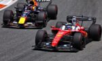 Three Formula 1 cars race in a tight pack on a track, led by a red Ferrari in the foreground.