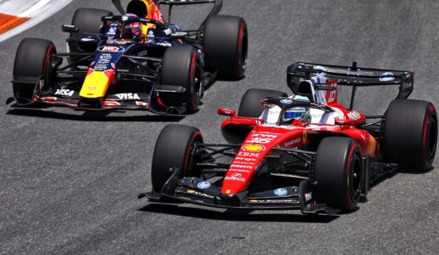 Three Formula 1 cars race in a tight pack on a track, led by a red Ferrari in the foreground.