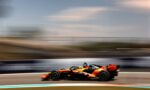 Orange Formula 1 car racing at high speed on a track, bumper-to-bumper motion blur in the background showing speed.
