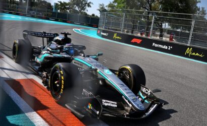 Formula 1 car taking a sharp turn on the Miami circuit, blue run-off and barriers along the track.