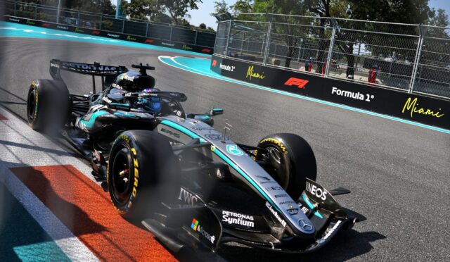 Formula 1 car taking a sharp turn on the Miami circuit, blue run-off and barriers along the track.