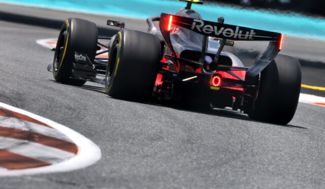 Rear view of a Formula 1-style race car taking a corner, red taillights illuminated, Revolut branding on the rear wing under bright track lighting.