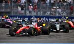 Race cars start a Grand Prix on a track with a cheering grandstand in the background, front red car leading the pack.