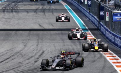 Formula 1 race on a street circuit with several cars closely following the lead car, barriers lining the track on the right side.