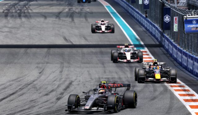 Formula 1 race on a street circuit with several cars closely following the lead car, barriers lining the track on the right side.