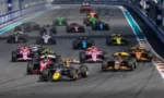 A pack of colorful Formula-style race cars accelerates from the starting line on a night race track.