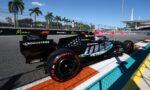 Mercedes Formula One car on the Miami street circuit, near the trackside barriers with palm trees and fencing in the background, blue sky above