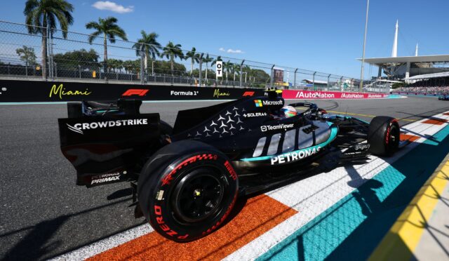Mercedes Formula One car on the Miami street circuit, near the trackside barriers with palm trees and fencing in the background, blue sky above