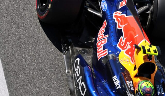 Close-up of a Red Bull racing F1 car on the track, showing blue and orange livery, sponsor logos, and front wing details.