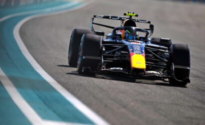 Formula 1 race car speeding around a curve on a race track, with teal run-off area on the left side