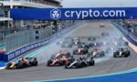 Formula 1 cars speeding off from the start on a blue-track circuit with sponsored barriers and a crowded grandstand above the track on crypto.com advertising.