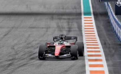 Red Ferrari Formula 1 car on track, close to orange-and-white striped runoff on the right.