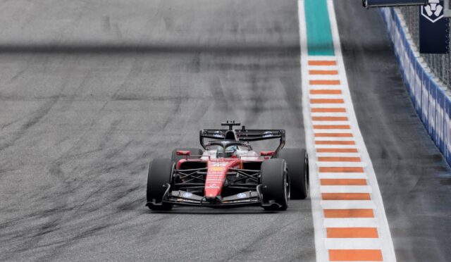 Red Ferrari Formula 1 car on track, close to orange-and-white striped runoff on the right.