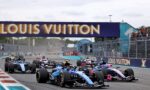 Group of Formula 1 cars at the race start beneath a Louis Vuitton banner, racing down the track with spectators along the barriers.