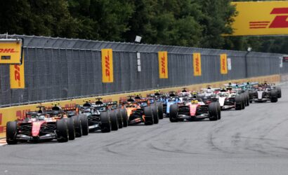 Row of Formula 1 race cars lined up on a straight track at the start of a race, DHL banners along the barrier behind them.