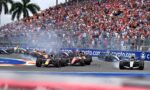 Formula 1 cars race side-by-side on a street circuit as a large crowd watches from grandstands behind a barrier, with smoke from tires and crypto.com advertising boards visible.