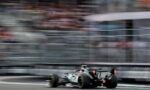 Formula 1 car speeding on a race track with heavy motion blur in the stands behind it.
