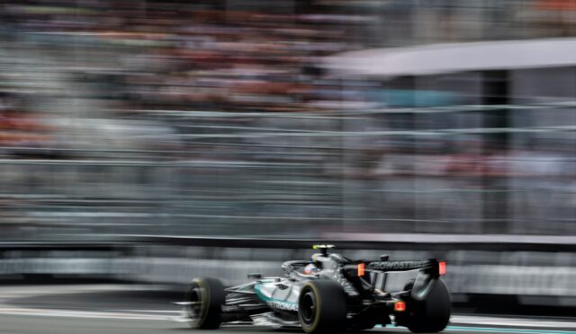 Formula 1 car speeding on a race track with heavy motion blur in the stands behind it.