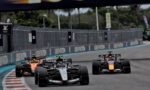 Four Formula 1 cars race closely on a slick street circuit, tires gripping the track as they speed toward a bend.