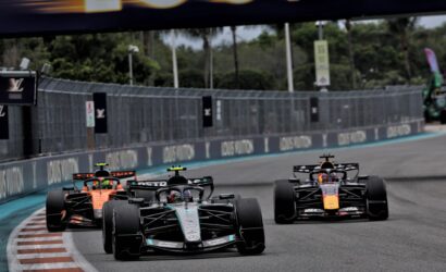 Four Formula 1 cars race closely on a slick street circuit, tires gripping the track as they speed toward a bend.