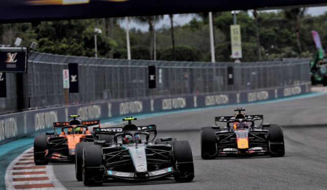 Four Formula 1 cars race closely on a slick street circuit, tires gripping the track as they speed toward a bend.