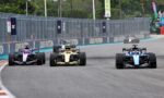Four Formula 1 cars race side by side on a track with Louis Vuitton banners along the barrier wall.
