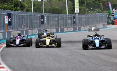 Four Formula 1 cars race side by side on a track with Louis Vuitton banners along the barrier wall.