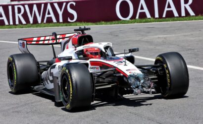 Open-wheel race car on a racetrack with a damaged nose and debris under the front, Qatar banner in the background.