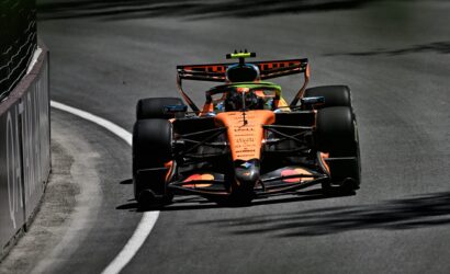 Orange Formula 1 car speeds along a curved race track, barrier on the left and the driver visible in the cockpit.