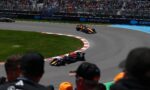 Orange Formula 1 car on a curved track with cheering spectators behind fencing and Salesforce banners?