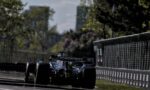 Formula 1 race car on a city street circuit, CrowdStrike branding on the rear wing near safety barriers.