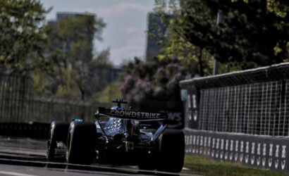 Formula 1 race car on a city street circuit, CrowdStrike branding on the rear wing near safety barriers.