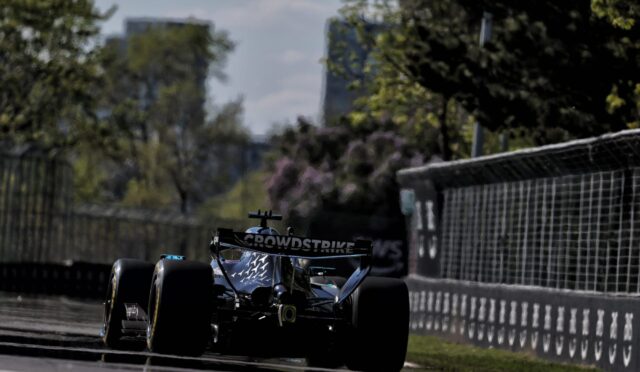 Formula 1 race car on a city street circuit, CrowdStrike branding on the rear wing near safety barriers.