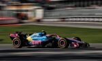 Colorful Formula 1 car with BWT livery speeding along a race track, motion blur background behind it.