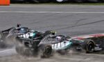 Mercedes Formula 1 cars from the Petronas team racing on a track, smoke and dust rising from the tires with sponsor logos visible