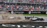 Two Formula 1 cars crash on a race track, kicking up dust as they slide near the barriers with a cheering crowd behind a chain-link fence and Motorola banners.