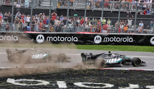Two Formula 1 cars crash on a race track, kicking up dust as they slide near the barriers with a cheering crowd behind a chain-link fence and Motorola banners.
