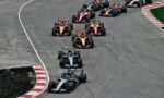 Multiple Formula 1 cars race in a tight group around a curved track, sponsor logos visible on the cars.