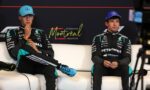 Two Mercedes F1 drivers sit on a white sofa during a press event, wearing team suits and blue caps, with a Montreal backdrop behind them and a red line above the logo.