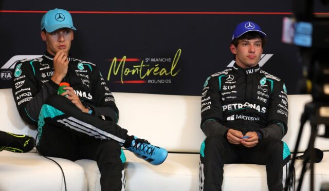 Two Mercedes F1 drivers sit on a white sofa during a press event, wearing team suits and blue caps, with a Montreal backdrop behind them and a red line above the logo.