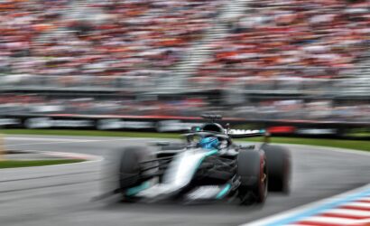 Blurred Formula 1 car racing on a track with a packed stadium in the background.