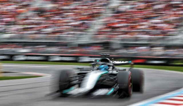 Blurred Formula 1 car racing on a track with a packed stadium in the background.