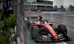 Ferrari Formula 1 car racing along a track with barriers and a grandstand in the background.