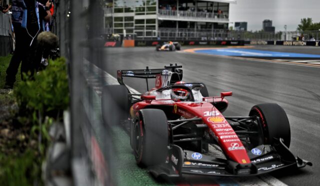 Ferrari Formula 1 car racing along a track with barriers and a grandstand in the background.