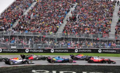 Crowded grandstands overlook a Formula 1 race with colorful race cars speeding along a track; Motorola banners line the barrier.