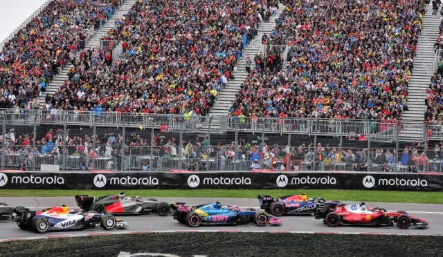 Crowded grandstands at a Formula 1 race with colorful spectators; race cars speed along the track with Motorola banners in the foreground.