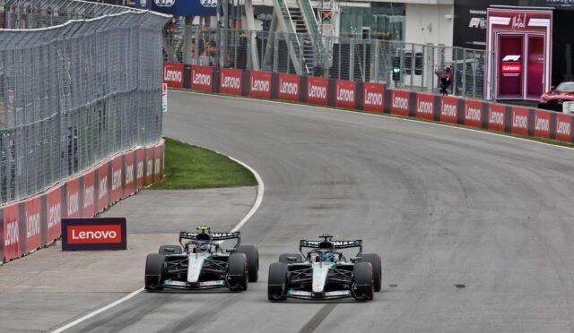 Two Mercedes Formula 1 cars racing on a track with red Lenovo barriers lining the wall.