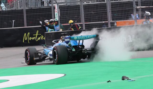 Blue Formula 1 car drifting with smoke near the pit wall, crew signaling in the background on a race track in Montreal.",