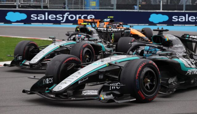 Three Formula 1 cars in a tight race, Mercedes–Petronas teal livery leading on a track with blue barriers in the background