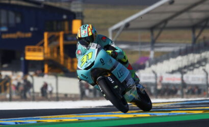 Moto racer leaning into a turn on a turquoise-blue race bike with number 97 and Leopard branding on a sunny track.
